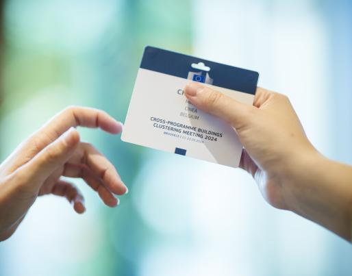 Two hands holding a credential of the event Cross-Programme Buildings Clustering Meeting 2024