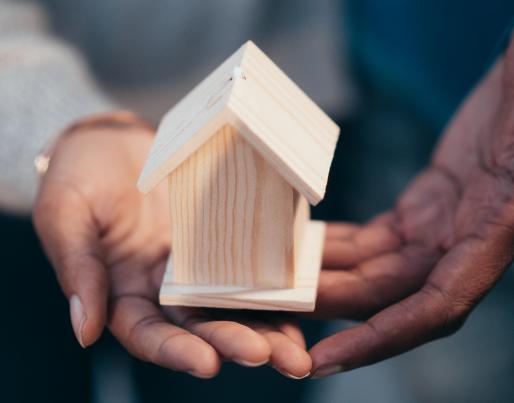 Hands holding a wooden model of a house