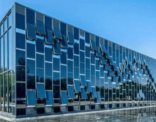 The image shows a modern building with a reflective glass façade and a geometric design. It is surrounded by trees, and a pond in front mirrors its structure.