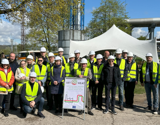 A group of people in high-visibility vests and hard hats in front of an industrial facility, gathered around a 'SET4HEAT' sign.