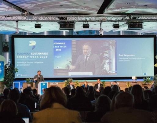 The image depicts a conference during European Sustainable Energy Week 2025, with Commissioner Dan Jørgensen speaking in front of a screen displaying the event’s theme.