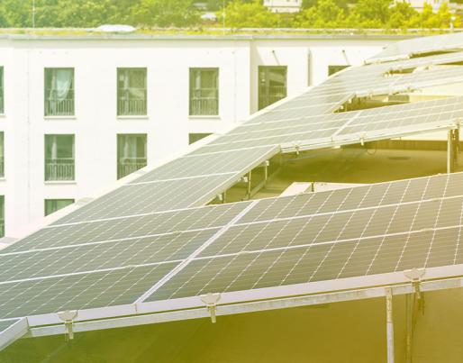 The image shows solar panels installed on the roof of a white building with windows. They are arranged in rows and capture sunlight to generate energy.