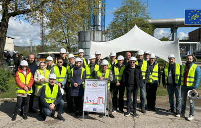 A group of people in high-visibility vests and hard hats in front of an industrial facility, gathered around a 'SET4HEAT' sign.