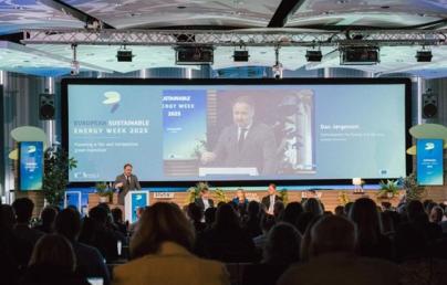 The image depicts a conference during European Sustainable Energy Week 2025, with Commissioner Dan Jørgensen speaking in front of a screen displaying the event’s theme.