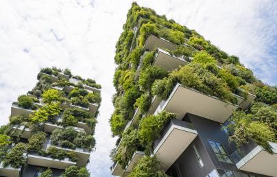 The image shows two tall buildings with balconies covered in plants and trees, forming a vertical forest. It is an example of green architecture that integrates vegetation to promote environmental sustainability.