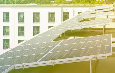 The image shows solar panels installed on the roof of a white building with windows. They are arranged in rows and capture sunlight to generate energy.