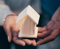 Hands holding a wooden model of a house