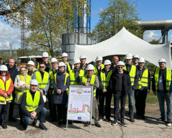 A group of people in high-visibility vests and hard hats in front of an industrial facility, gathered around a 'SET4HEAT' sign.